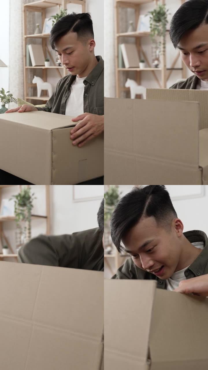 垂直视频: 快乐的韩国男顾客坐在沙发上打开包裹纸箱的包装对在家通过邮政运输的赠品包装感到惊讶和满意
