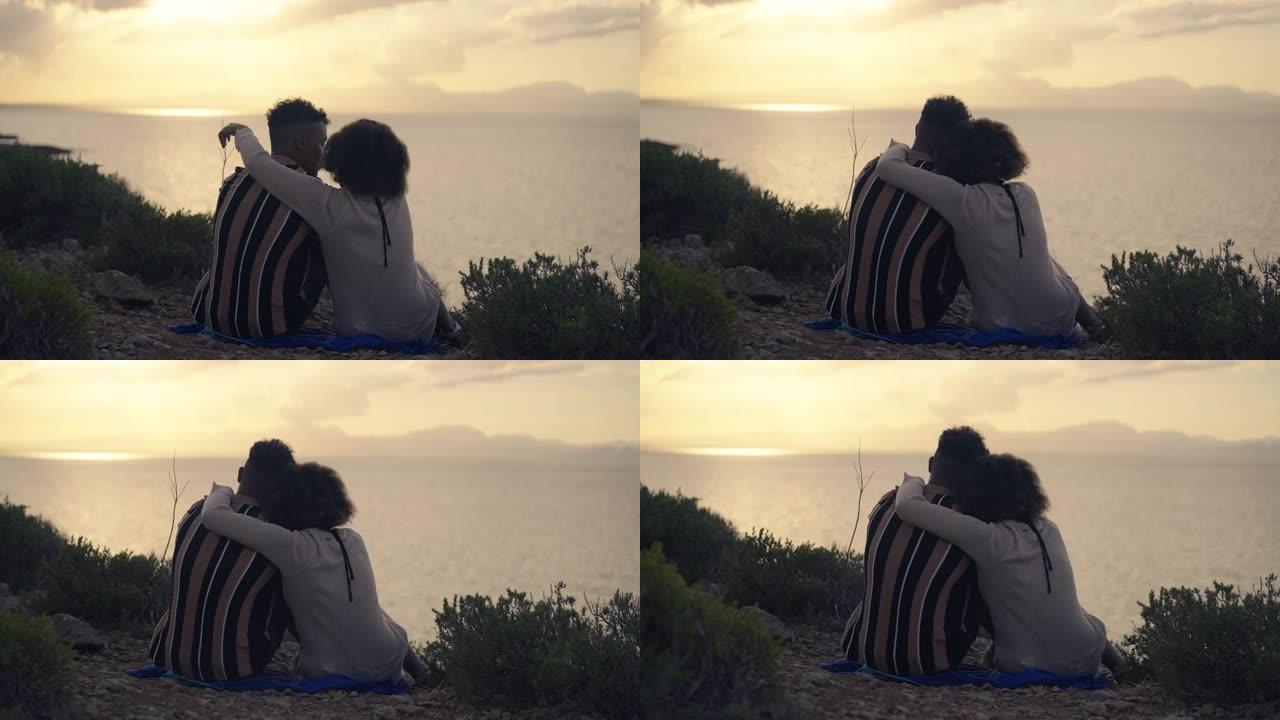 非洲族裔情侣一起坐在悬崖上。浪漫的日落