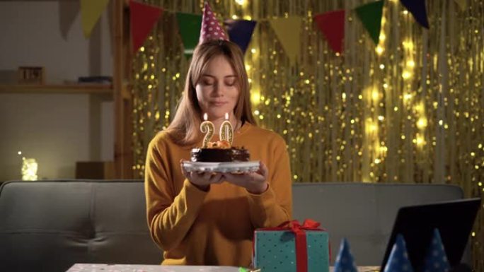 20岁生日。年轻女子在生日蛋糕上吹蜡烛。20周年纪念数字。女孩拿着蛋糕许愿