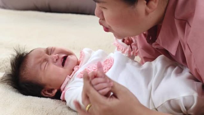 亚洲新生婴儿妈妈躺在米色床上，可爱的婴儿早上醒来后哭泣，蹒跚学步的孩子饿了要牛奶。婴儿托儿所用床上用