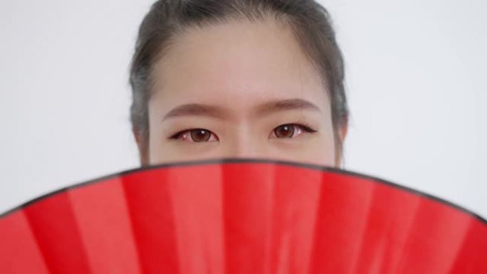 中国/亚洲美女脸特写春节红扇遮住脸上半部分，看着镜头…