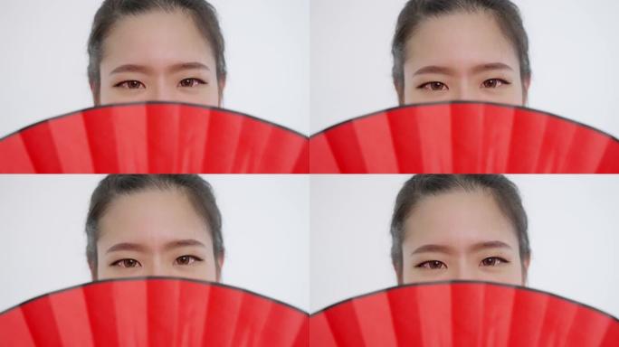 中国/亚洲美女脸特写春节红扇遮住脸上半部分，看着镜头…