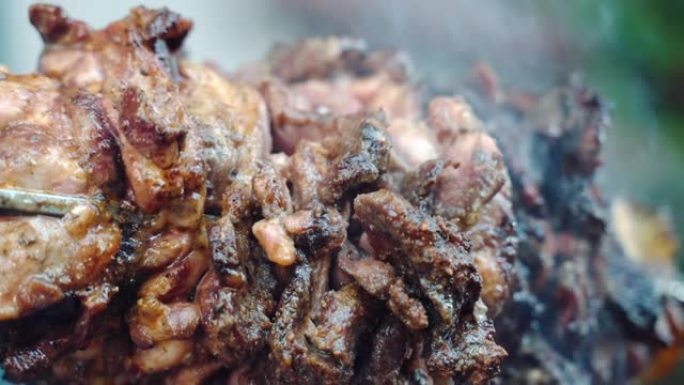 肉串在燃烧的火上烘烤和吸烟，多汁的肉块与脆皮在火上缓慢旋转，自制的调味肉里脊肉在烧烤吸烟者，为野餐派