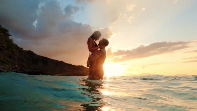 暑假浪漫的异性恋夫妇。在金色日落时温柔地拥抱在绿松石水中