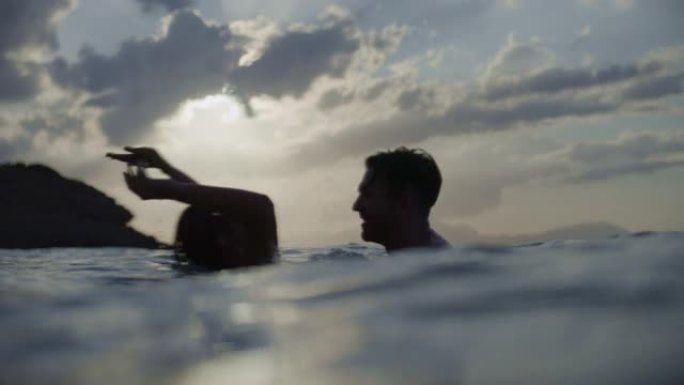 浪漫的异性恋夫妇在金色日落时在海里游泳。在水中玩耍和拥抱