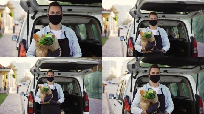 一名送货员戴着防护口罩的动作镜头，上面拿着食品杂货站在街上的户外。电晕病毒或COVID 19流行或大