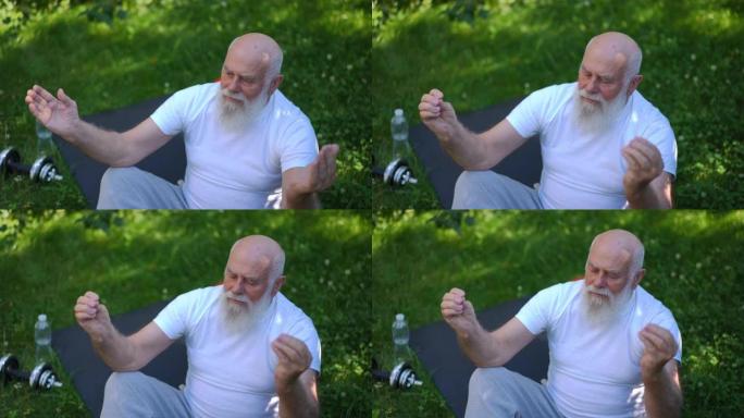 高角视图的老高加索大胡子男人在莲花姿势冥想坐在运动垫上，以慢动作闭上眼睛。平静自信的高级瑜伽士在夏季