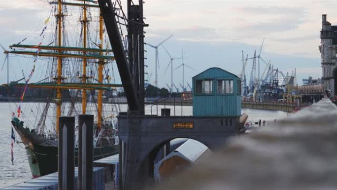 经典帆船在帆船节期间停泊在老港口起重机旁边，背景是风力涡轮机