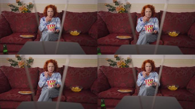 吸收高加索复古女人切换频道吃爆米花在家看电视。前视图美丽的红发女士坐在沙发上，在20世纪80年代20