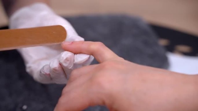 女性美容大师使用一次性手套制作合适形状的指甲，专业美容艺术家准备客户的指甲进行修指甲，美容院修指甲程