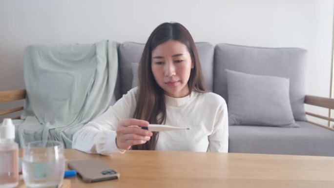 年轻的亚洲病人妇女拿温度计，亚洲女性在家里客厅测量体温，人们医疗保健和医疗