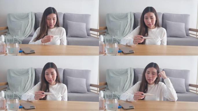 年轻的亚洲病人妇女拿温度计，亚洲女性在家里客厅测量体温，人们医疗保健和医疗