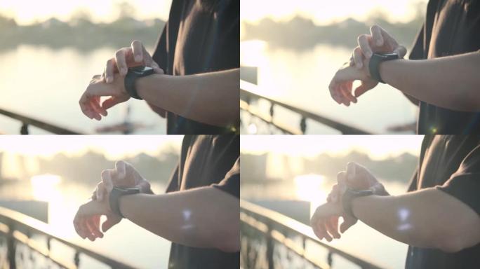 亚洲男性在早晨日出时在公园跑步进行锻炼，使用智能手表按start记录并观察心率以保持健康。