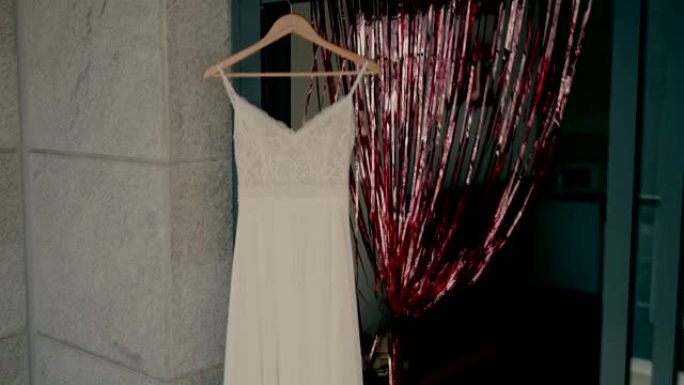新娘的礼服挂在门口的衣架上，石墙旁边有花环