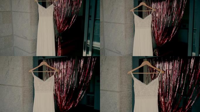 新娘的礼服挂在门口的衣架上，石墙旁边有花环