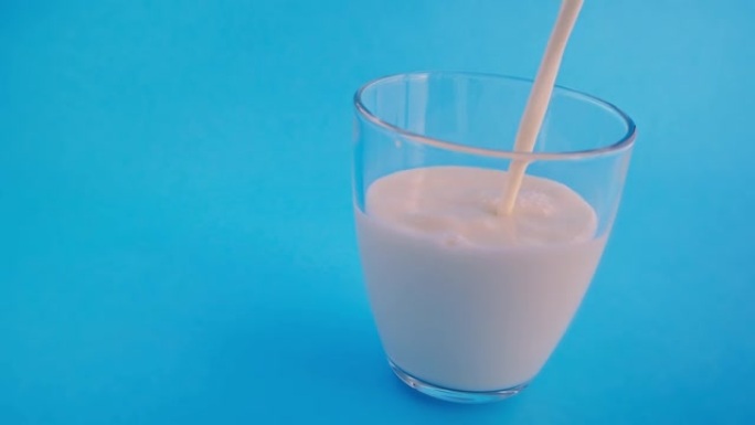 将新鲜的天然牛奶倒入淡蓝色背景的透明玻璃杯中。