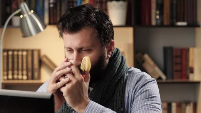 感冒男子在办公室或公寓的工作场所慢慢喝柠檬热茶，吃柠檬片。感冒流感治疗概念