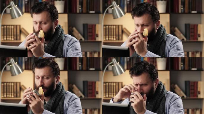 感冒男子在办公室或公寓的工作场所慢慢喝柠檬热茶，吃柠檬片。感冒流感治疗概念