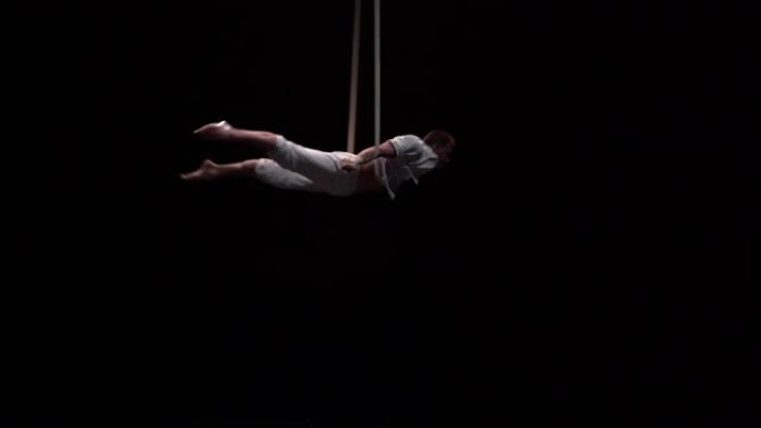 空中绑带上的男性肌肉马戏团艺术家在黑色背景上的空中表演强有力的技巧
