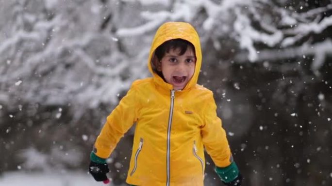 穿着黄色冬装的有趣小男孩在降雪时行走。孩子们的户外冬季活动。