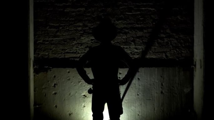 一个男人的剪影把帽子戴在头上，把双手放在臀部，靠在砖墙的背景上