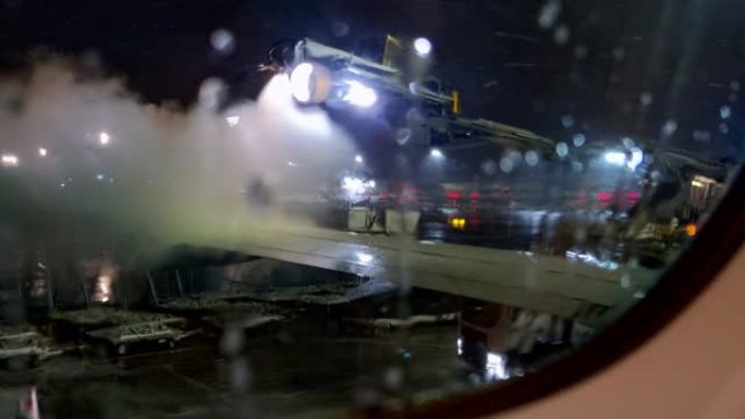 飞机在暴风雪下晚上起飞前除冰。从机舱窗户内部看到机翼上的防冰喷雾。
