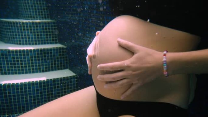 一个沉重的孕妇将腹部抱在水下
