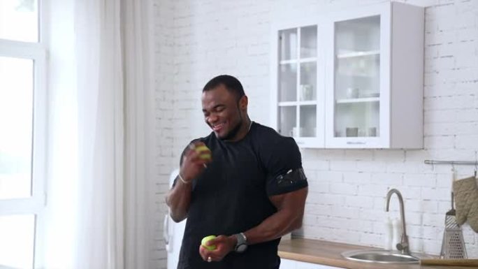 快乐的年轻多种族男子在厨房背景下慢跑苹果，选择性聚焦，特写。节食概念。健康人扔水果