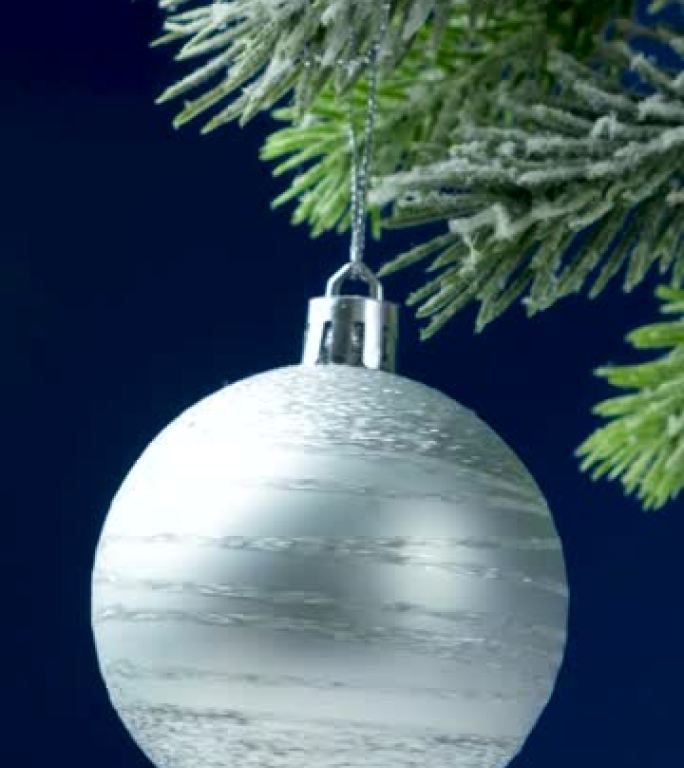 一个闪亮的白球在白雪覆盖的圣诞树上旋转，垂直视频