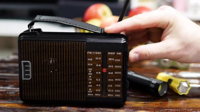 一个人在旧木桌上的收音机上调谐无线电波。带天线的古董接收器。按比例调谐模拟收音机。一个人在旧收音机里