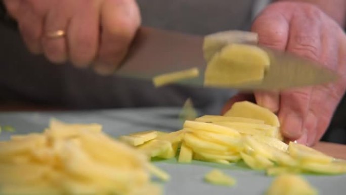 厨师在桌子上切美味的土豆做饭。健康食品。老人在木板上切土豆的手的特写。雄性切新鲜的生土豆。用刀准备蔬