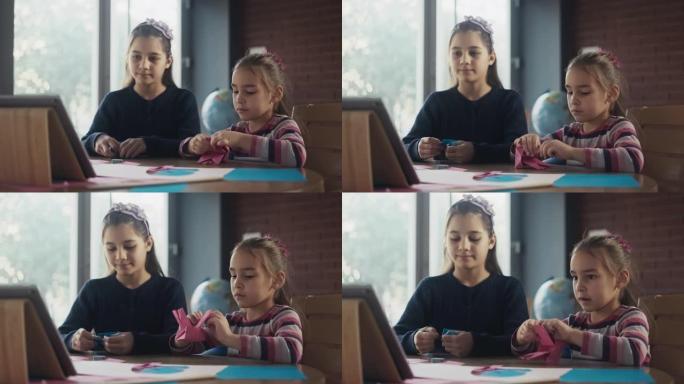 儿童姐妹使用彩纸做折纸玩具，按照笔记本电脑视频教程中的步骤操作