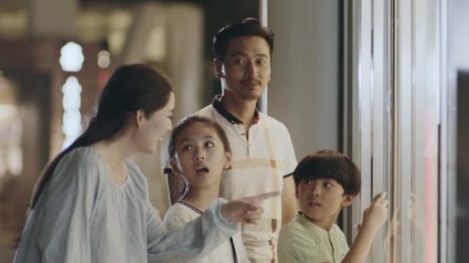 亚洲家庭父母和孩子站着看着购物中心的窗户
