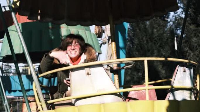 开朗的成熟女人坐在阳光明媚的冬季公园的摩天轮机舱里向某人挥手