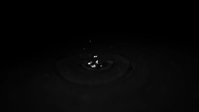 水滴在黑色背景上的水面上破裂。慢动作