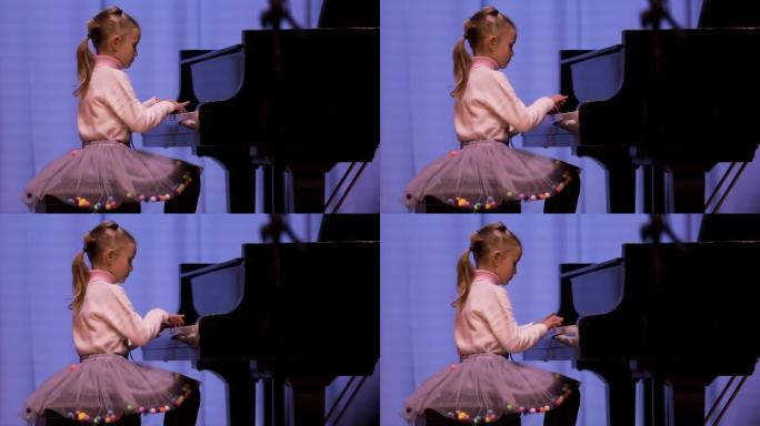 可爱的7岁女孩在彩色拱腹的灯光下在舞台上演奏钢琴。在音乐学校度过休闲的一天