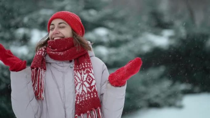 4k慢动作摄像机跟踪拍摄的快乐漂亮女人穿着红色手套和帽子在下雪天在冷杉树林里散步，在寒假玩雪