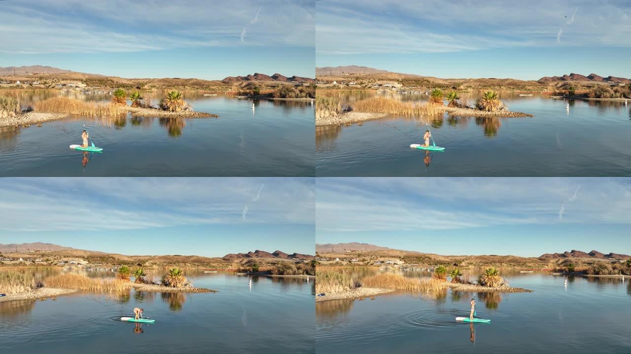 年轻女子在宁静的湖上的站立桨板 (SUP) 上放松