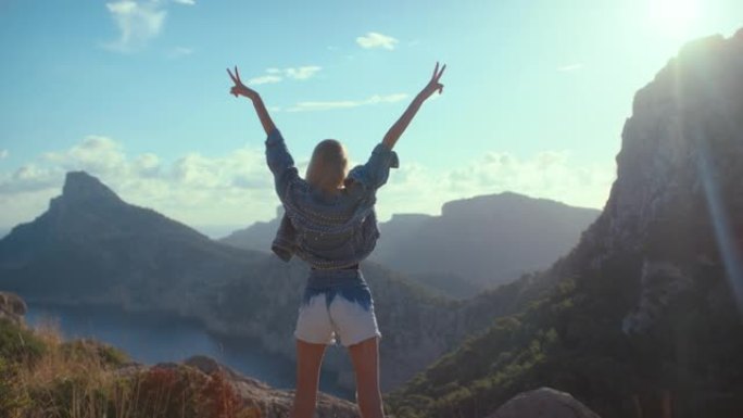 征服山脉。山顶上的女人举起手来庆祝一次成功的徒步旅行