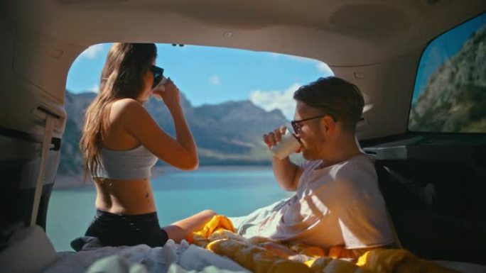 亲爱的夫妇在湖边的一个大汽车后备箱里休息和露营。欣赏湖景，一起喝茶