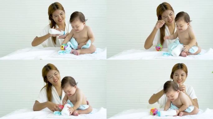 可爱的女婴在妈妈洗澡后在身上涂上爽身粉，妈妈在床上给她的小女儿涂上粉粉，梳理她的女婴的头发