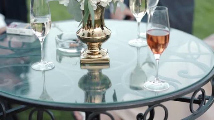 优雅的公司派对在令人惊叹的花园里，有圆形玻璃桌子和鲜花花束，同事放松，喝独家酒，聊天和享受派对。周末