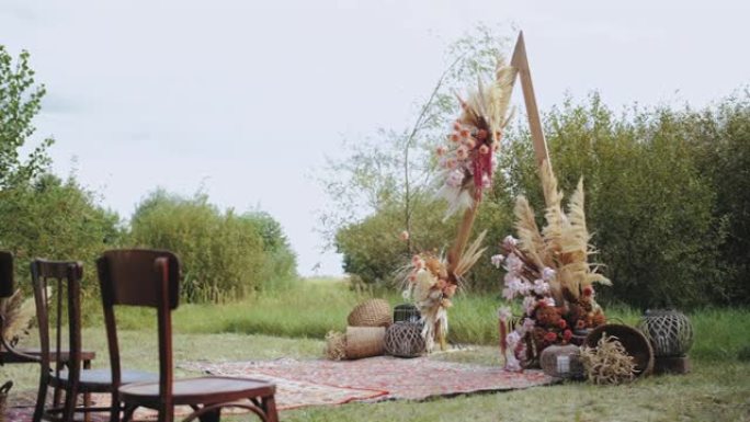户外婚礼上美丽的波西米亚拱门装饰。柔和色彩的花卉组合物，干花，木椅和老式地毯。夏季婚礼。