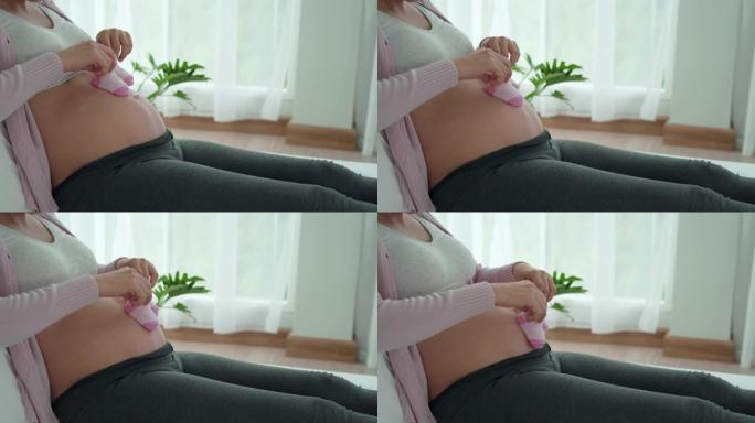 女人拿着准备好的粉红色鞋子在肚子上玩耍。鞋子是新生儿配件的一部分。孕妇的概念活动和放松以减少抑郁。