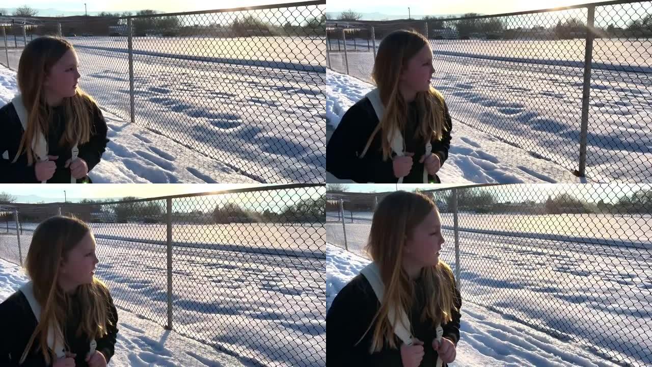 8-9岁的女孩在雪中沿着链节围栏从学校走回家