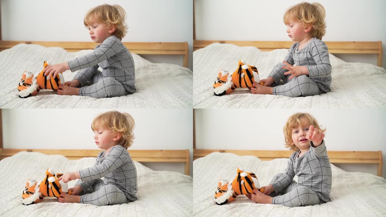 两岁的小男孩在舒适的房间里的床上和玩具老虎玩耍