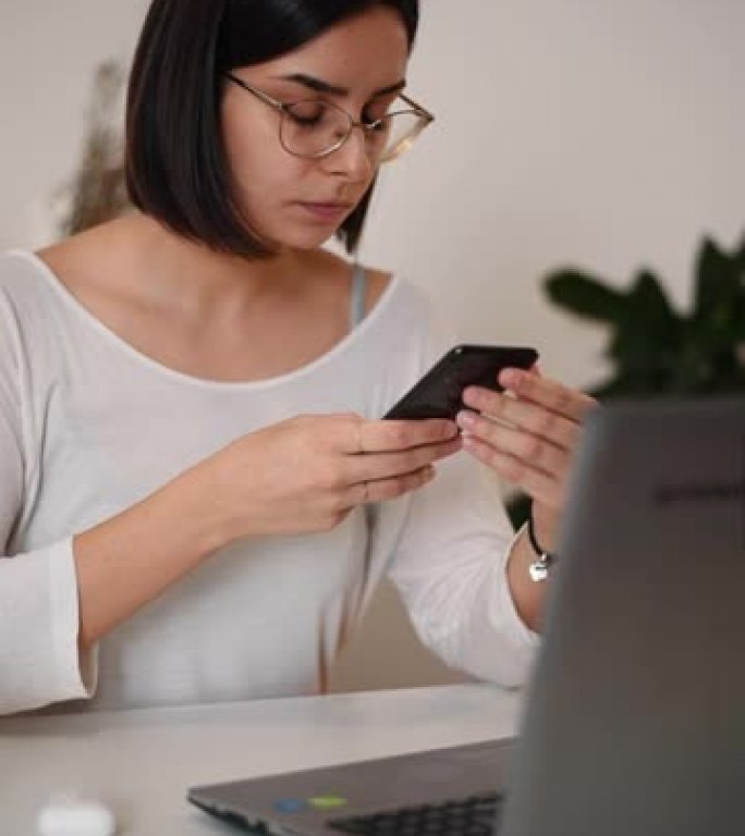 女人在使用笔记本电脑和在家工作时在智能手机上键入消息