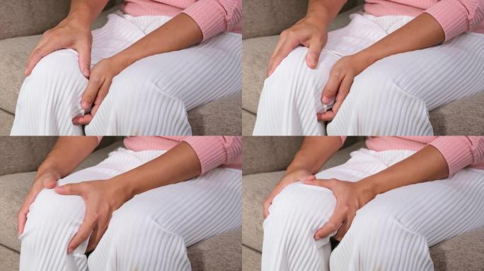 女人在家按摩痛苦的膝盖的特写镜头。坐在沙发上患有膝盖疼痛的女人。医疗保健和医疗概念。