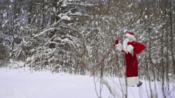 圣诞老人带着魔法杖和一袋圣诞礼物走在雪林里。