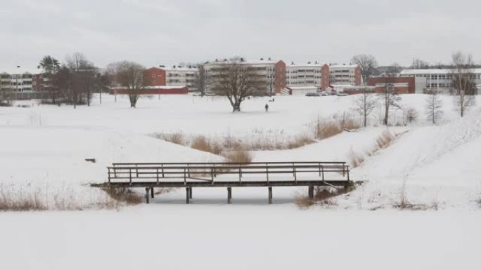 鸟瞰一个人走在积雪覆盖的田野里，后面有建筑物